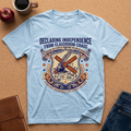 Light blue t-shirt with a graphic design on a brown surface with a coffee cup, apple, and jeans.