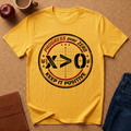 Yellow t-shirt with motivational design on a brown surface with an apple, coffee cup, and jeans. shirt Says "Progress over Zero, Keep it Positive." surrounding "X>0" the math inequality. 