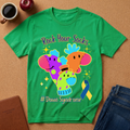 A bright green graphic t-shirt laid flat on a cork background, featuring colorful cartoon socks and the text 'Rock Your Socks' and '# Down Syndrome'. A coffee mug, apple, notebook, and jeans are styled around it.