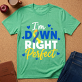 Heather Green T-Shirt says "I'm Down Right Perfect" with a Down Syndrome ribbon and blue hearts on a cork background.