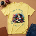 Yellow T-Shirt says "THE PURSUIT OF KNOWLEDGE" with a pile of colorful books graphic and watercolor styling overspray. 