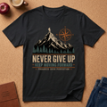 Black T-Shirt Graphic of a man hiking on a Mountain next to a compass symbol rising out of a pine forest.  Underneath it reads "Never Give Up, Keep Moving Forward, Progress over Perfection"