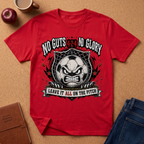 A red short-sleeve graphic T-shirt laid flat on a cork-like surface, surrounded by props including an apple, a mug, a notebook, and folded blue jeans. The shirt features a large distressed black-and-white soccer-ball face graphic with the text 'NO GUTS NO GLORY' above and 'LEAVE IT ALL ON THE PITCH' below.