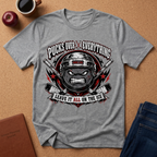 A heather gray graphic t-shirt laid flat on a cork background, featuring a hockey-themed design with crossed sticks, a helmeted face, and the text 'PUCKS OVER EVERYTHING' and 'LEAVE IT ALL ON THE ICE'.