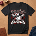 A black short-sleeve graphic t-shirt laid flat on a cork background, featuring a baseball-themed design with the text 'Swing or Strike' and 'No Fear at the Plate'. The shirt is styled with props including an apple, a coffee cup, a journal, and jeans.