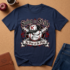 A navy blue graphic t-shirt laid flat on a brown cork-like surface, surrounded by lifestyle props including an apple, a coffee cup, a brown journal, and blue jeans. The t-shirt features a baseball-themed graphic with the text 'Swing or Strike' and 'No Fear at the Plate'.