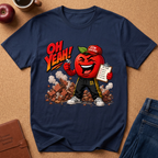 A navy blue graphic t-shirt laid flat on a cork background, featuring a cartoon red apple character dressed as a gym teacher with the text 'OH YEAH!' and a clipboard.