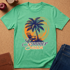 A green short-sleeve graphic T-shirt laid flat on a cork surface, featuring a palm tree, chair, and the words 'Summer Season' in orange and purple. Surrounding props include an apple, coffee cup, brown journal, and blue jeans.