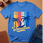 A blue short-sleeve graphic T-shirt laid flat on a cork background, featuring the words “SUMMER Vacation” with palm tree silhouettes and a retro striped background. Styled flat-lay props include a brown journal, a cup, an apple, and blue jeans.
