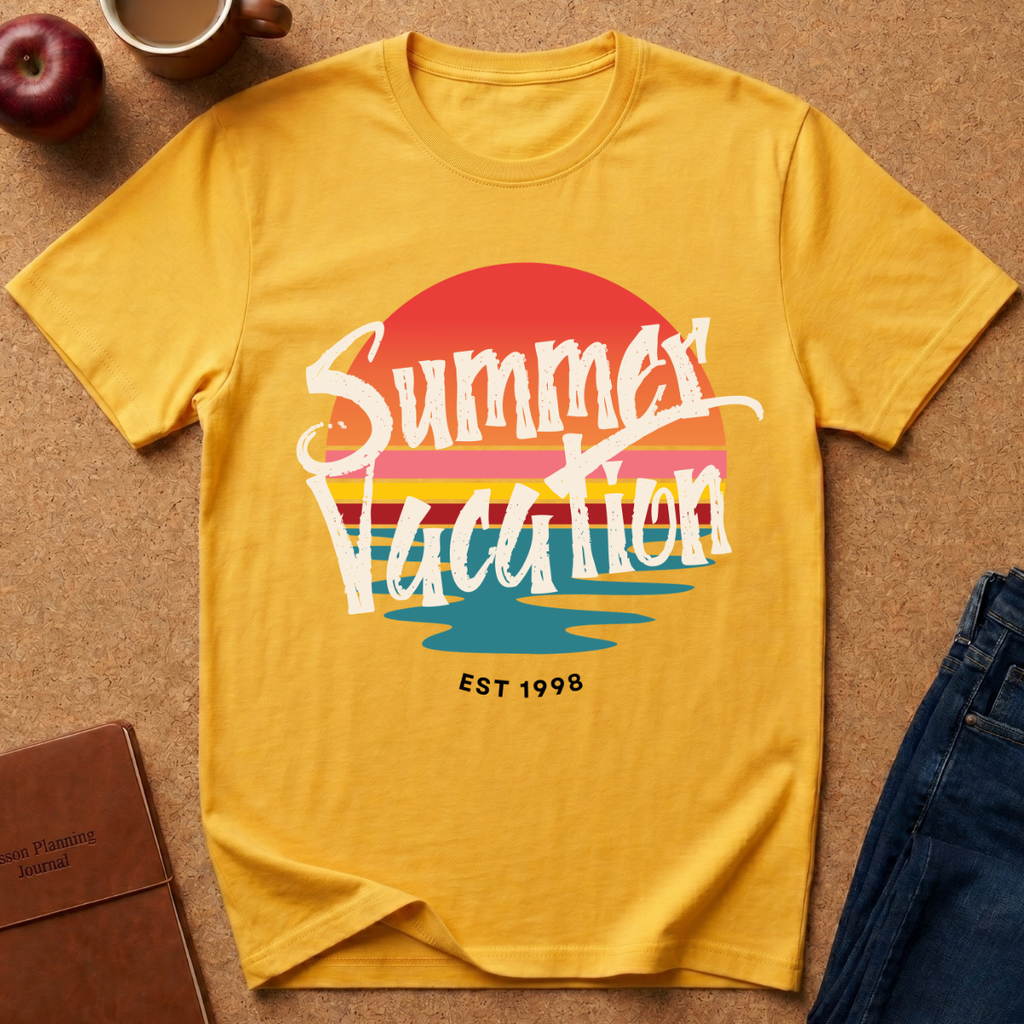 A yellow short-sleeve graphic T-shirt laid flat on a tan surface, with a retro sunset-style print reading “Summer Vacation” and “EST 1998.” Surrounding props include part of a red apple, a coffee cup, a brown notebook, and blue jeans.