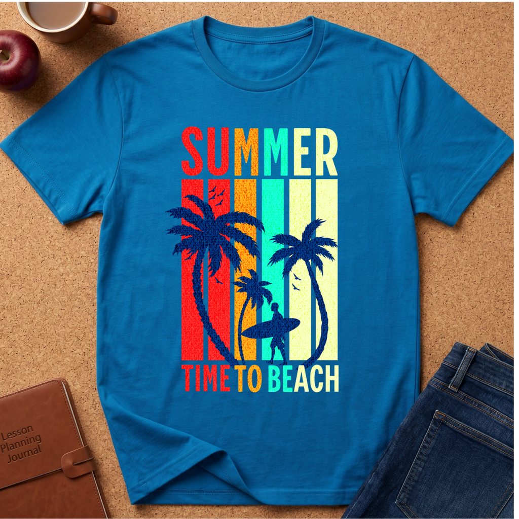 A bright blue short-sleeve t-shirt laid flat on a cork surface, featuring a retro vertical-striped graphic with palm trees and the words 'SUMMER TIME TO BEACH' in multicolor lettering. Surrounding props include an apple, a coffee cup, a brown journal, and folded blue jeans.