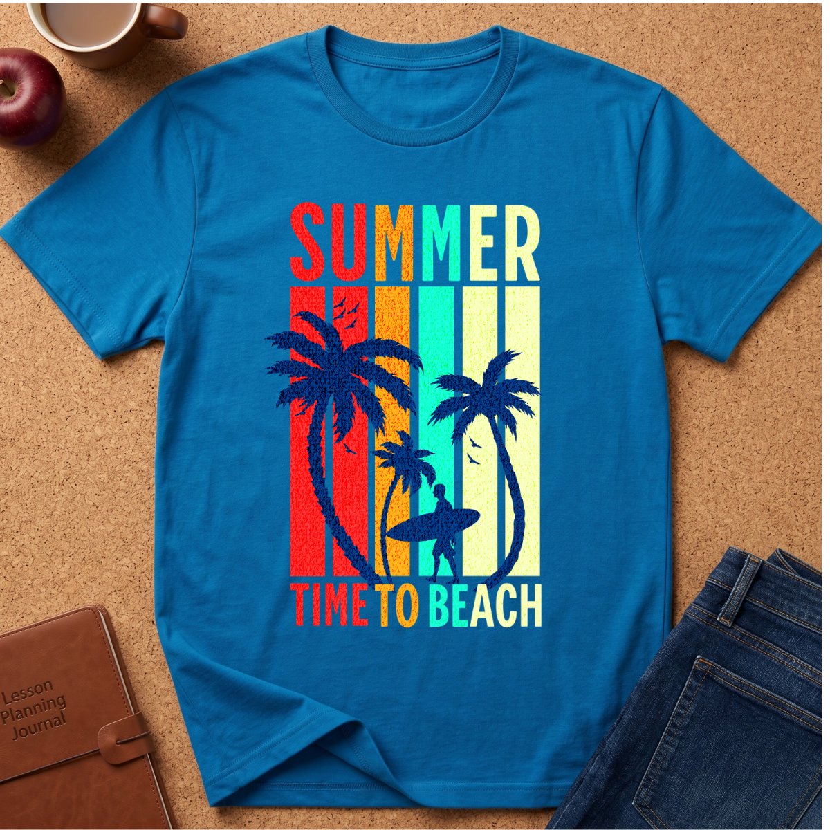 A bright blue short-sleeve t-shirt laid flat on a cork surface, featuring a retro vertical-striped graphic with palm trees and the words 'SUMMER TIME TO BEACH' in multicolor lettering. Surrounding props include an apple, a coffee cup, a brown journal, and folded blue jeans.