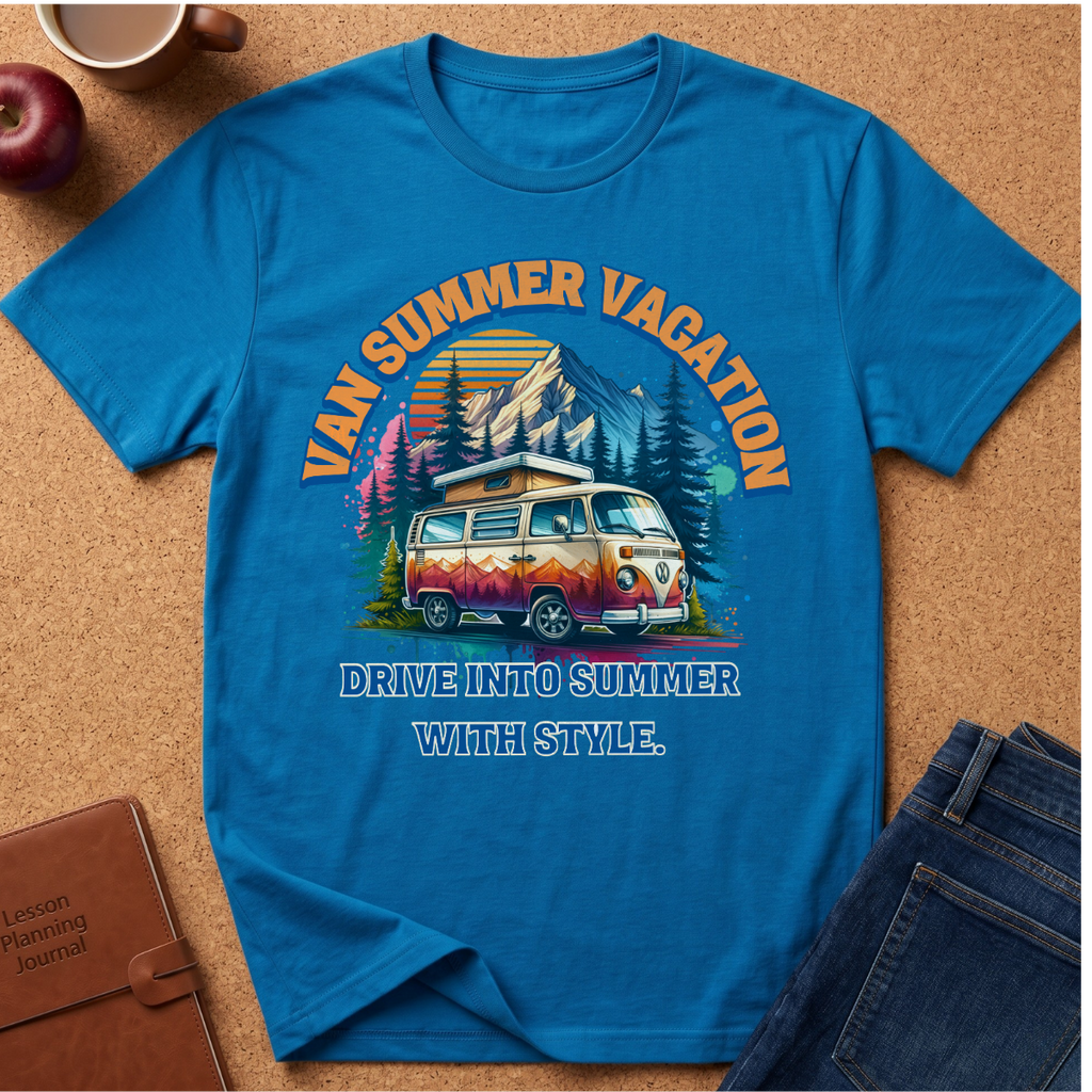 A bright blue graphic t-shirt laid flat on a cork background, featuring a retro-style illustration of a vintage van with mountains, trees, and the text 'VAN SUMMER VACATION' and 'DRIVE INTO SUMMER WITH STYLE.' Surrounding props include an apple, a coffee cup, a brown journal, and folded blue jeans.