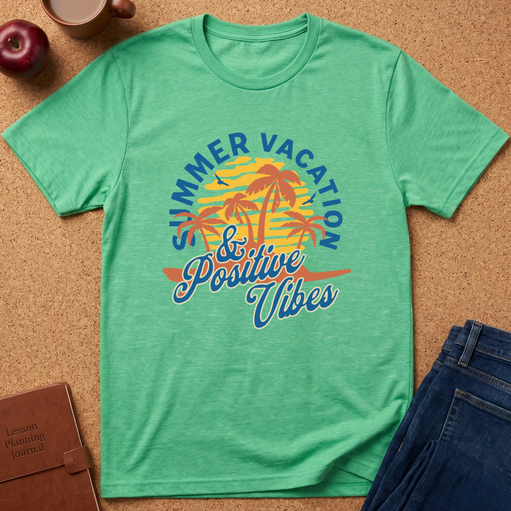 A green short-sleeve t-shirt laid flat on a cork background, featuring a colorful retro graphic with palm trees and the text 'Summer Vacation & Positive Vibes.' Props around it include an apple, a coffee cup, a notebook, and folded blue jeans.
