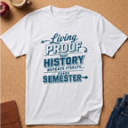 A white short-sleeve graphic T-shirt laid flat on a cork background, with blue text reading 'Living PROOF THAT HISTORY REPEATS ITSELF.