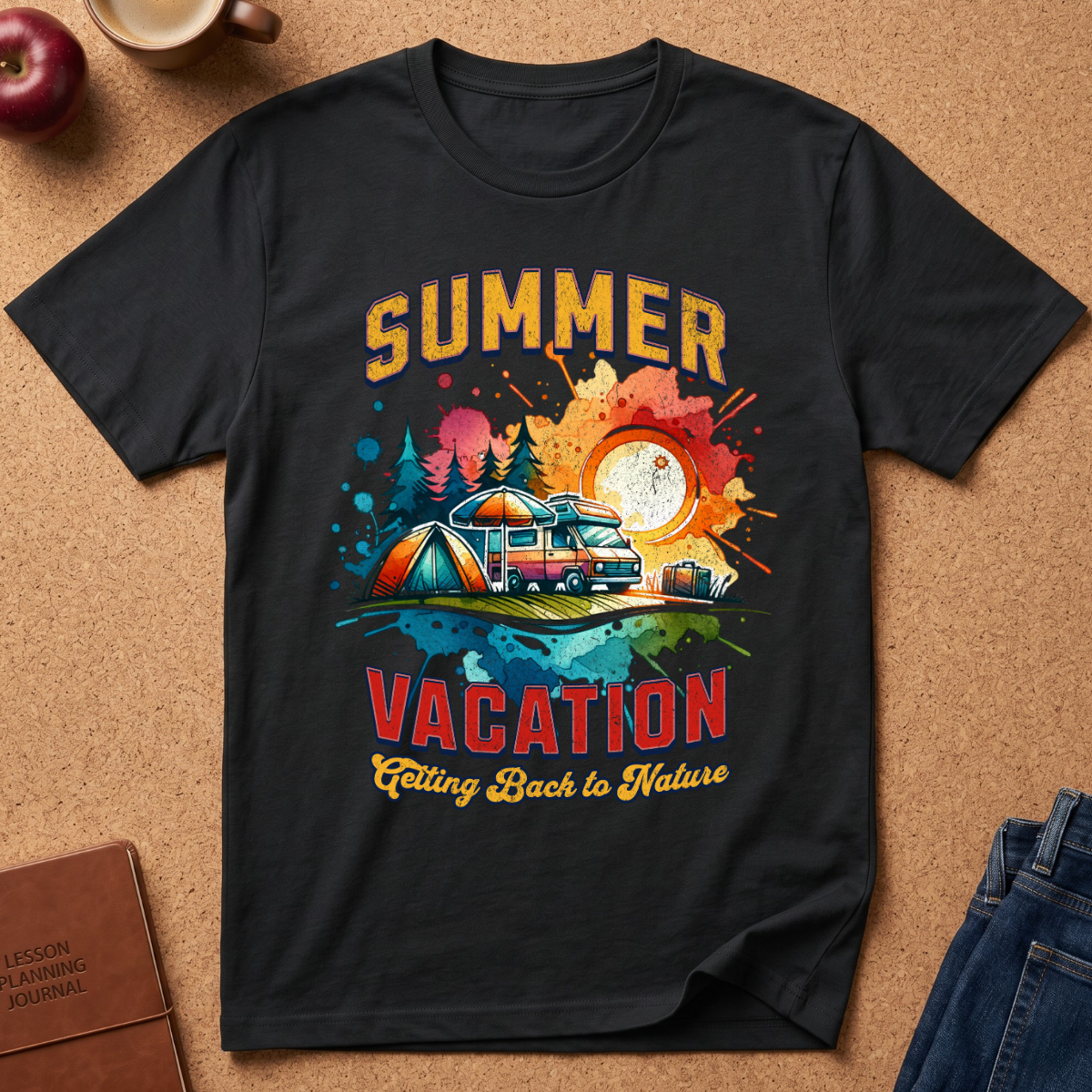 A black short-sleeve graphic T-shirt laid flat on a cork-like surface, featuring a colorful summer vacation camping design with a tent, camper van, trees, and the text 'SUMMER VACATION Calling Back to Nature.' Partial props around it include an apple, a mug, a journal, and jeans.