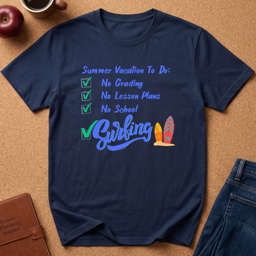 A navy blue graphic t-shirt laid flat on a cork board background, featuring a checklist design for summer vacation with 'No Grading', 'No Lesson Plans', 'No School', and 'Surfing' in blue script alongside two colorful surfboards. Partial jeans, an apple, a coffee cup, and a journal are visible around the shirt as styled props.