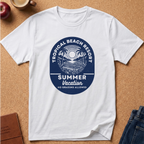 A white short-sleeve crewneck t-shirt laid flat on a cork background, featuring a circular blue graphic print that reads 'TROPICAL BEACH RESORT SUMMER Vacation NO GRADING ALLOWED' with palm trees and a sun.