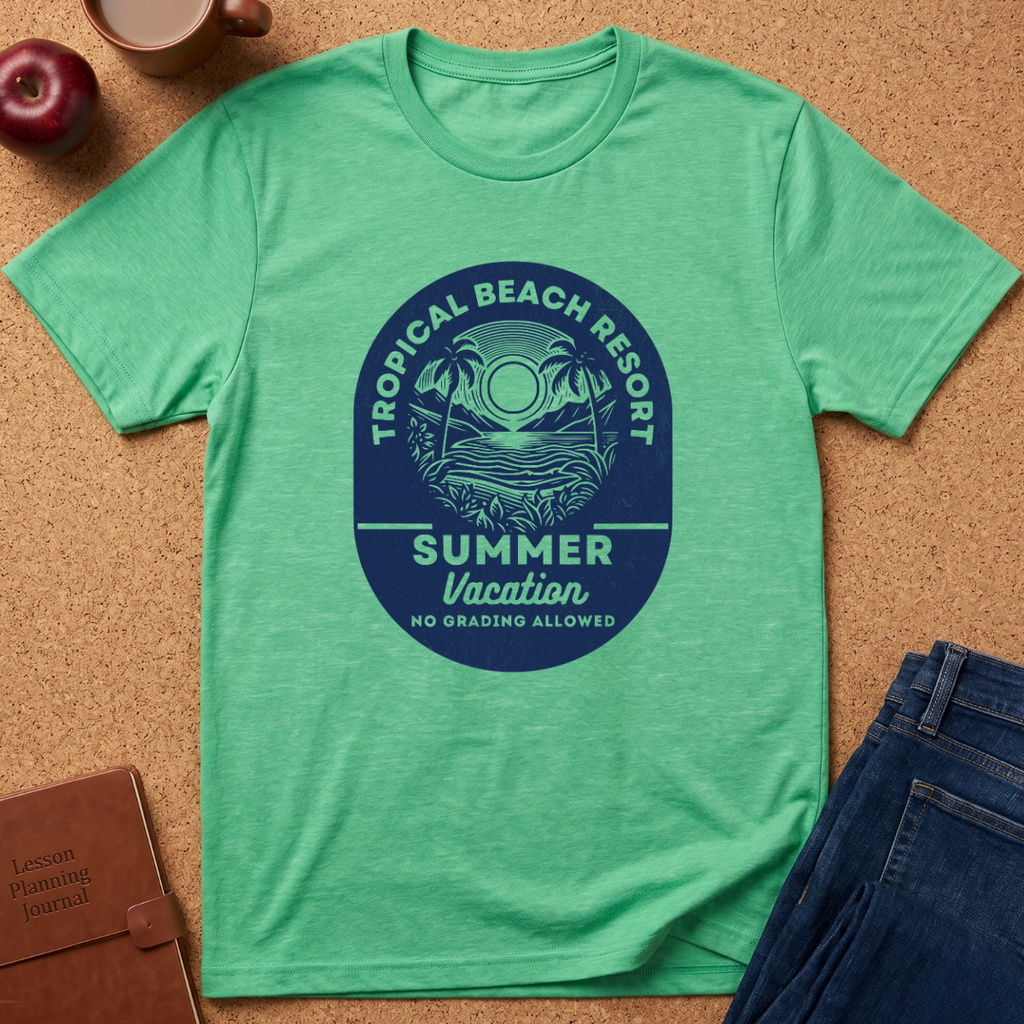 A heather green short-sleeve t-shirt laid flat on a cork surface, featuring a large circular blue graphic on the chest that reads 'TROPICAL BEACH RESORT SUMMER Vacation NO GRADING ALLOWED' with palm trees and a sun. A red apple, coffee cup, brown journal, and blue jeans are partially visible around it as styling props.
