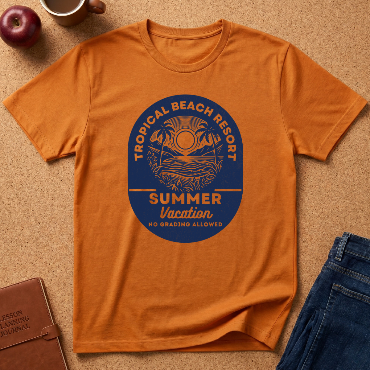 An orange short-sleeve t-shirt with a blue circular graphic reading 'Tropical Beach Resort Summer Vacation No Grading Allowed', laid flat on a cork surface with an apple, mug, notebook, and jeans nearby.