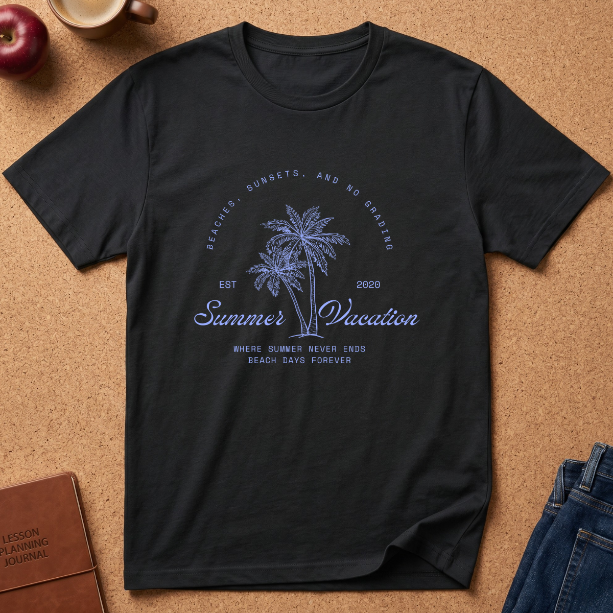A black short-sleeve graphic t-shirt laid flat on a cork background, featuring a blue palm tree design with the text 'Summer Vacation' and beach-themed phrases. Styled flat-lay props include an apple, a coffee mug, a journal, and blue jeans.