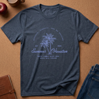 A heathered navy blue t-shirt with a light blue graphic print featuring palm trees and the text 'Summer Vacation' laid flat on a cork background with lifestyle props.