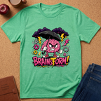 A mint green short-sleeve t-shirt laid flat on a cork background, featuring a colorful graphic of an angry pink brain holding a black umbrella with the text 'BRAINSFORM!'.