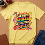 A yellow short-sleeve t-shirt with a colorful retro-style graphic reading 'Straight Outta Summer Break' surrounded by rainbow, smiley face, apple, notebook, pencil, and bow details, laid flat on a cork-like surface with jeans, a coffee cup, and a notebook nearby.