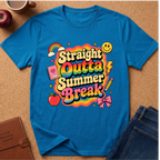 A bright blue graphic T-shirt laid flat on a cork surface, surrounded by styled props including an apple, coffee cup, notebook, and jeans. The shirt features a large colorful retro-style text graphic reading 'Straight Outta Summer Break' with rainbow, smiley face, lightning bolt, notebook, apple, pencil, and bow tie illustrations.