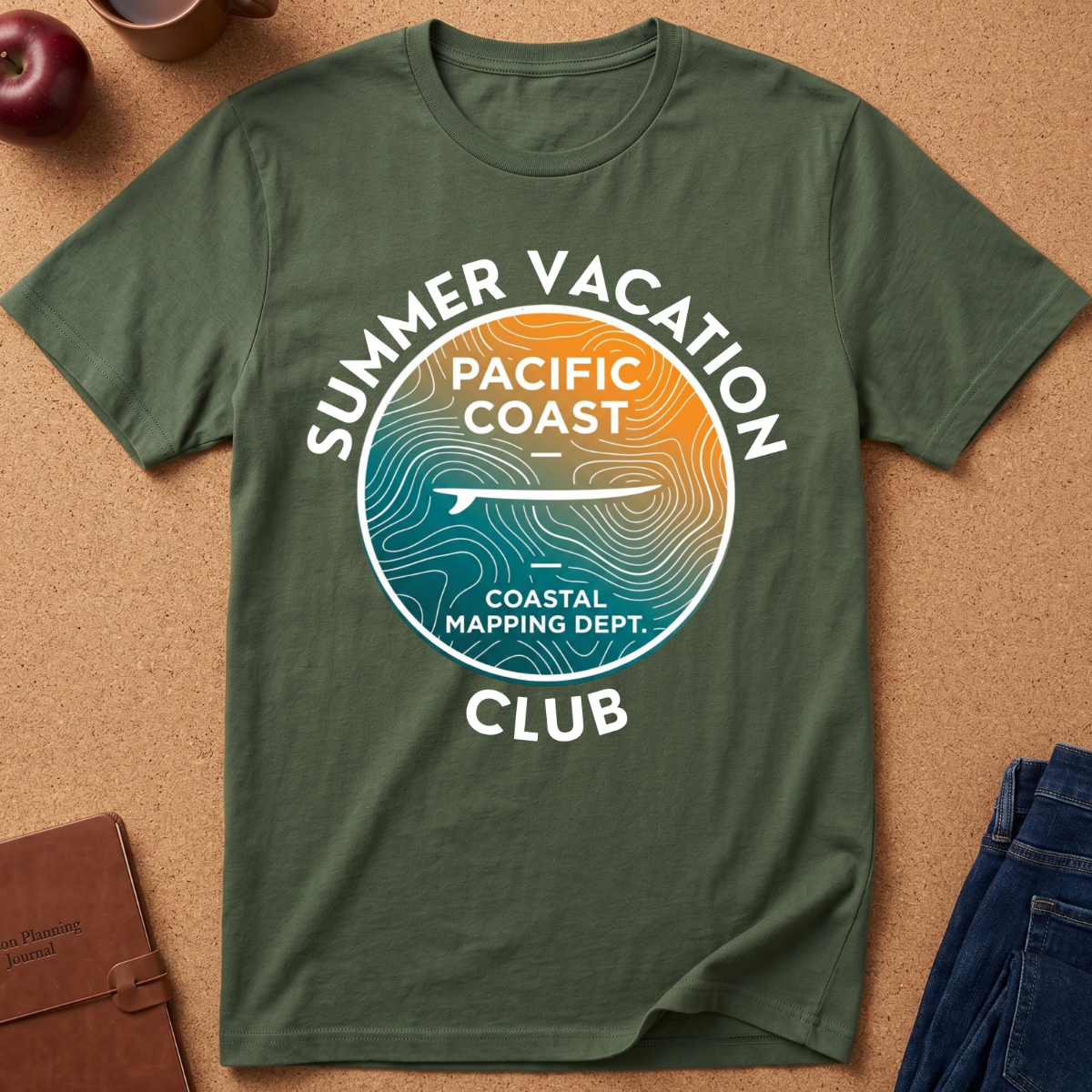 An olive green short-sleeve t-shirt laid flat on a cork background, featuring a circular graphic with the text 'SUMMER VACATION PACIFIC COAST COASTAL MAPPING DEPT. CLUB' and a topographic map design in blue, teal, and orange.