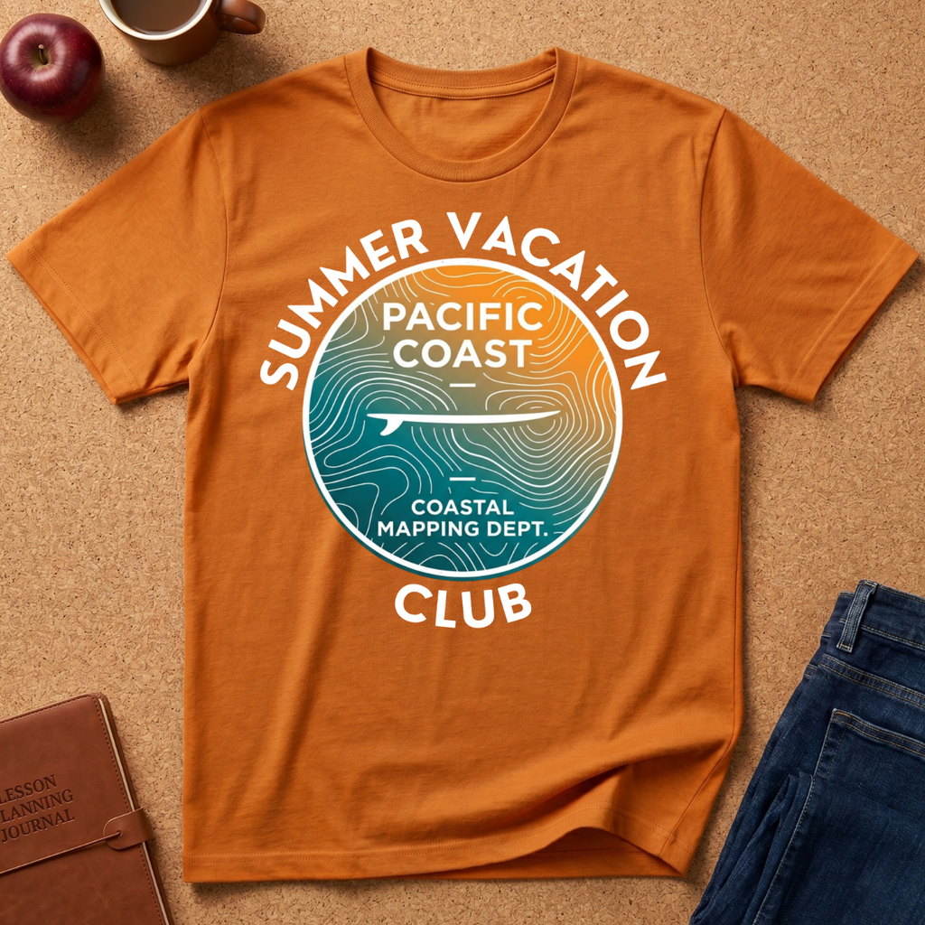 An orange short-sleeve graphic T-shirt laid flat on a cork surface, with a circular coastal-themed print reading “Summer Vacation Pacific Coast Club” and “Coastal Mapping Dept.” Blue jeans, a notebook, a mug, and a red apple are partially visible around it as styling props.