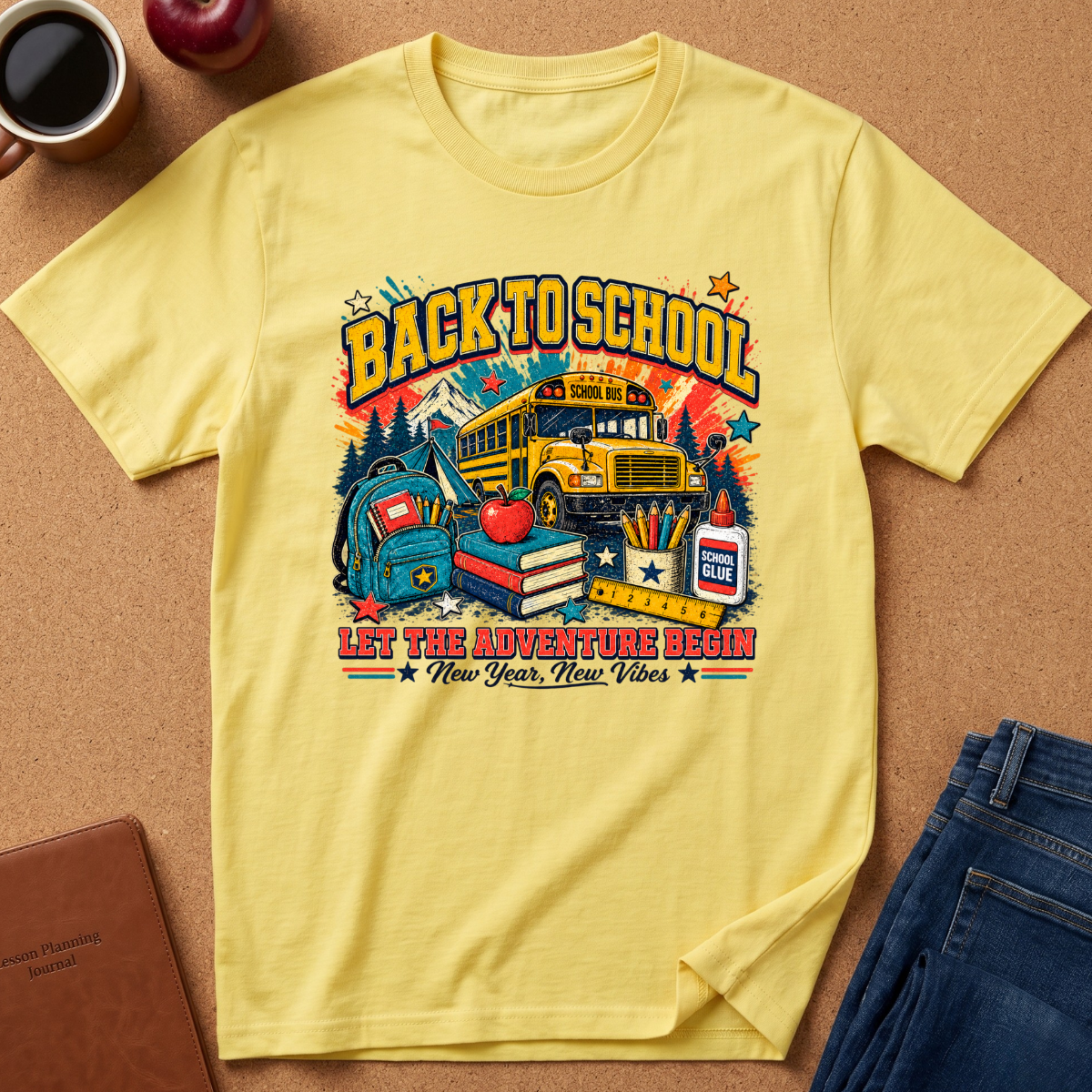 A yellow short-sleeve graphic T-shirt laid flat on a cork surface, surrounded by lifestyle props including a coffee mug, apple, notebook, and jeans. The shirt features a cocan you rewrite my description and seo in my brand voice?lorful 'Back to School' school bus and books graphic with the text 'Let the adventure begin New Year, New Vibes'.