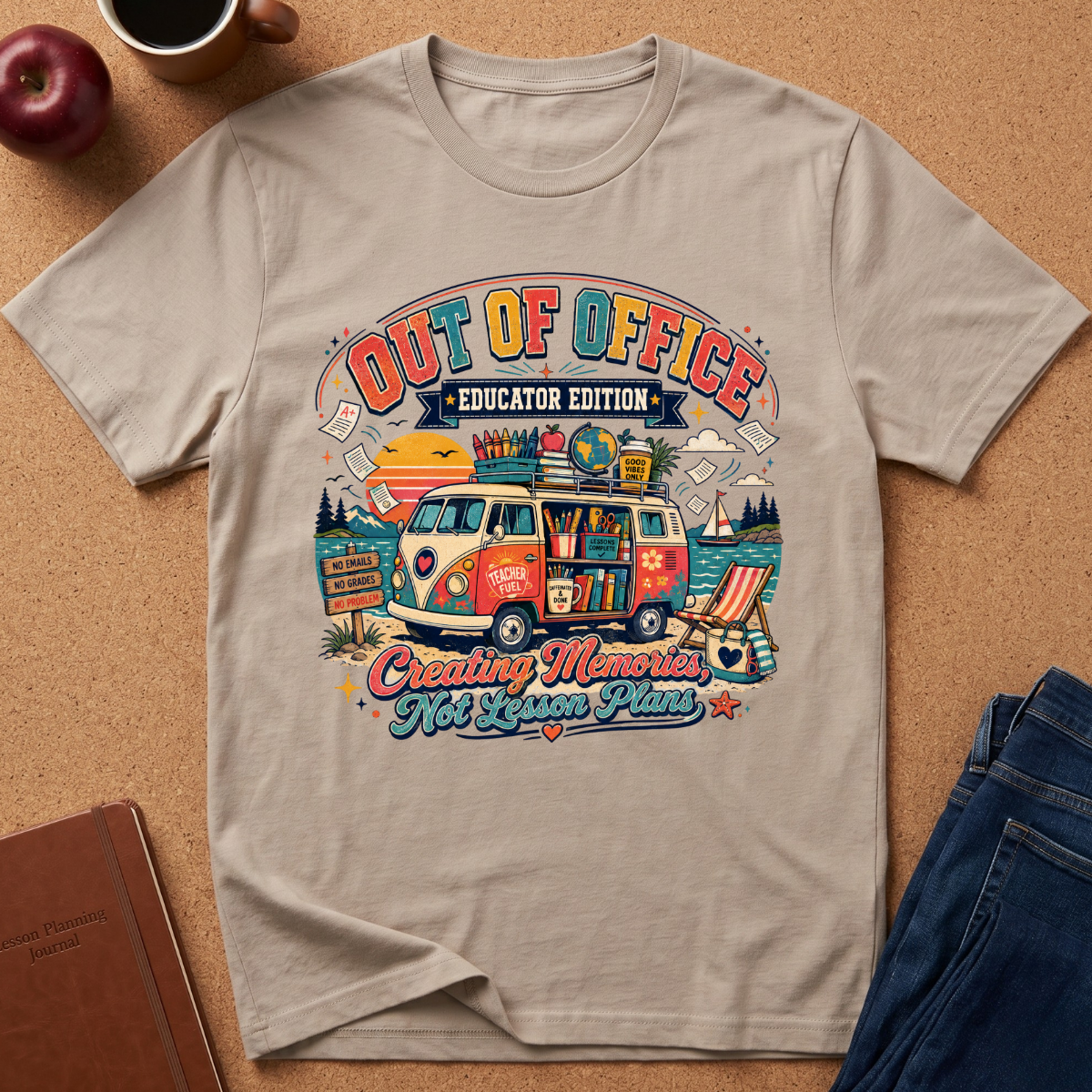 A beige graphic t-shirt laid flat on a cork background, featuring a colorful retro-style illustration of a camper van with the text 'OUT OF OFFICE EDUCATOR EDITION' and 'Creating Memories Not Lesson Plans.' Styled flat-lay props include an apple, coffee cup, notebook, and jeans.