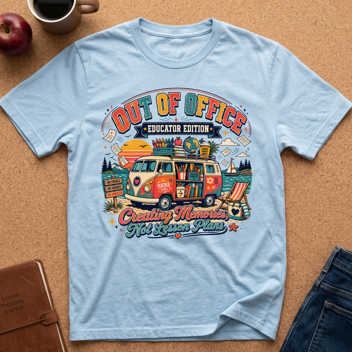 A light blue graphic t-shirt laid flat on a cork background, featuring a colorful retro-style illustration of a van with books and the text 'OUT OF OFFICE EDUCATOR EDITION' and 'Creating Memories Not Lesson Plans'.