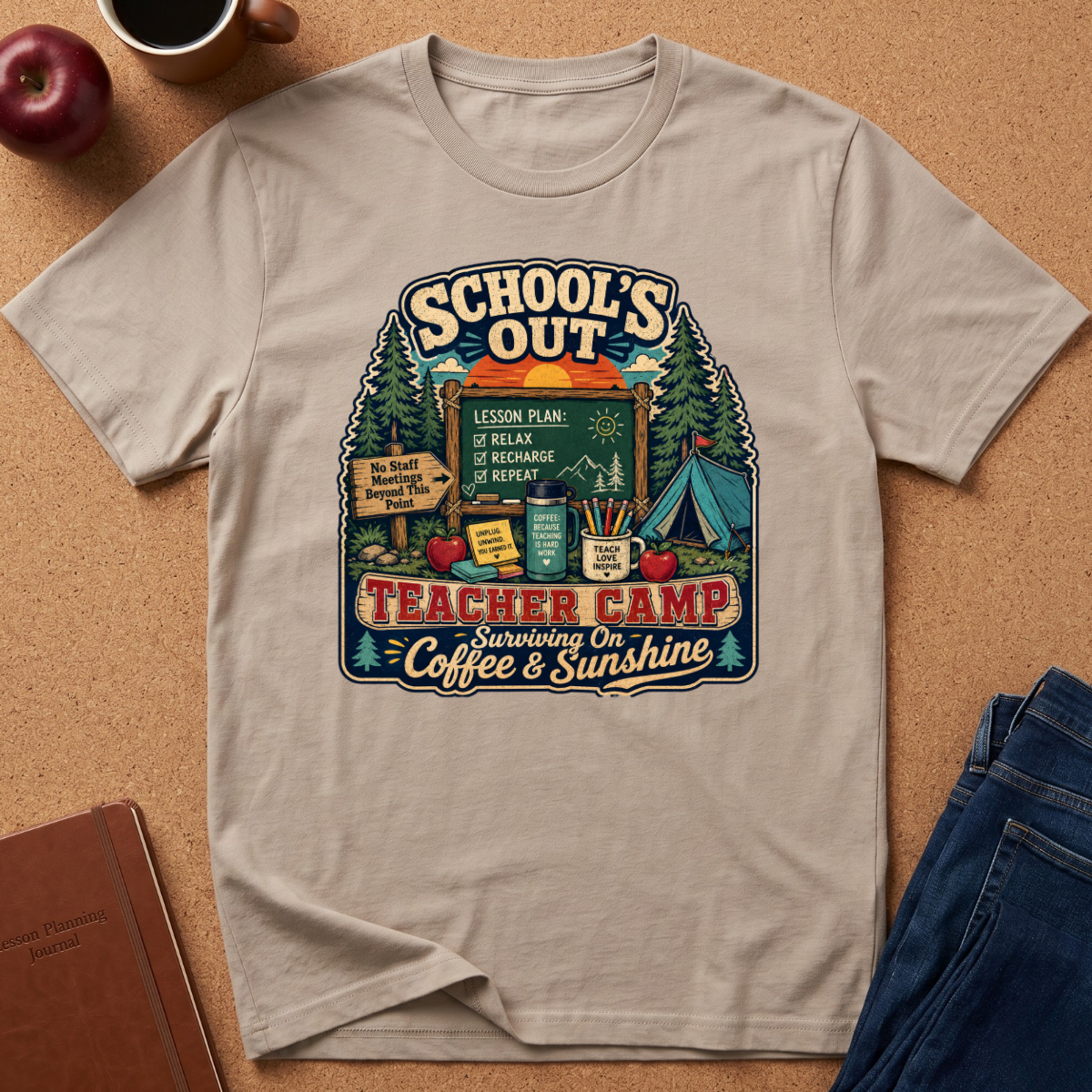 A beige graphic t-shirt laid flat on a cork background, surrounded by lifestyle props including an apple, a coffee cup, a notebook, and a pair of jeans. The t-shirt features a colorful retro-style graphic with camping and school-themed illustrations and the text 'SCHOOL'S OUT TEACHER CAMP Surviving On Coffee & Sunshine'.