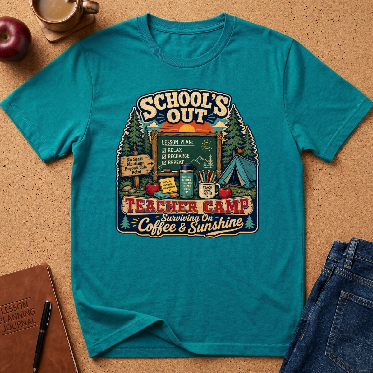 A teal short-sleeve graphic T-shirt laid flat on a cork surface, surrounded by styled props including a coffee cup, apple, notebook, pen, and jeans. The shirt features a large retro-style teacher-themed camp graphic with the text 'School's Out Teacher Camp' and 'Surviving on Coffee & Sunshine.