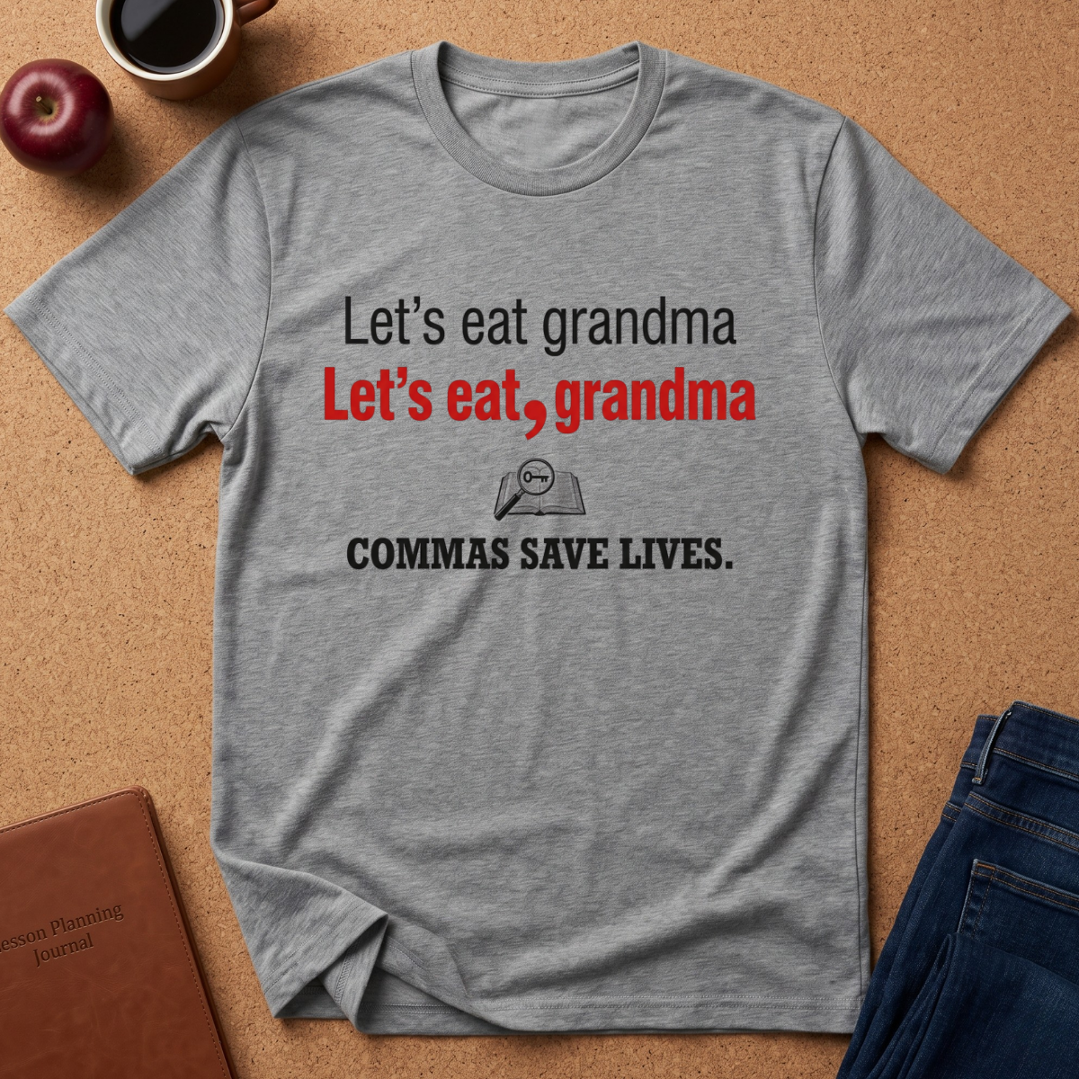 A heather gray graphic t-shirt laid flat on a cork background, featuring the text 'Let's eat grandma' in black and red, with a small magnifying glass graphic and 'COMMAS SAVE LIVES.' in black below.