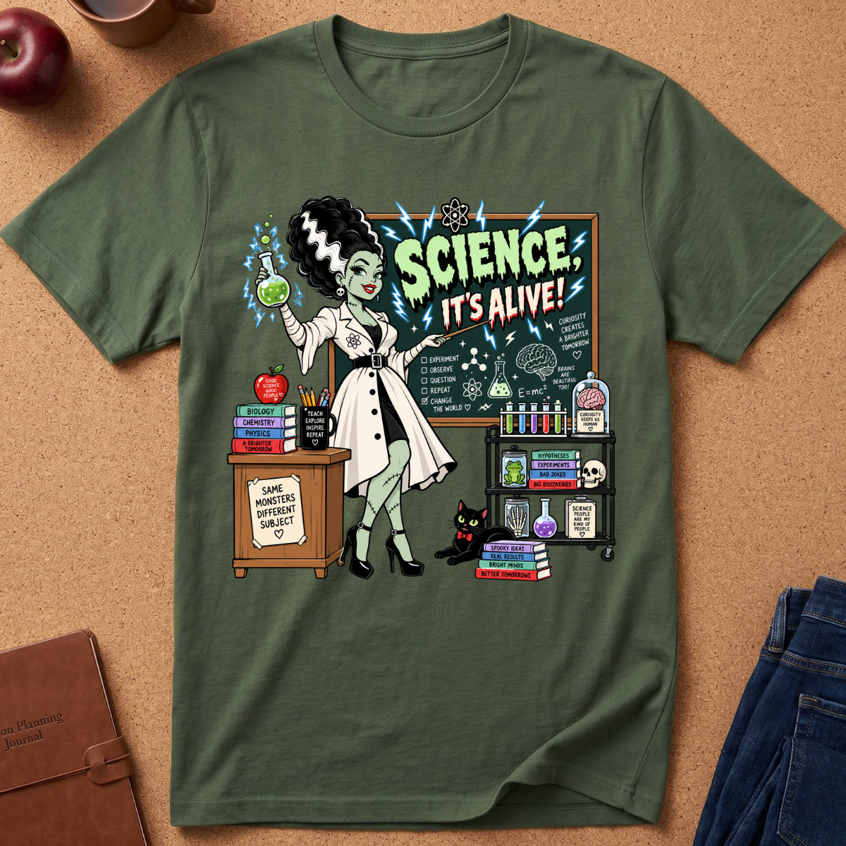 An olive green short-sleeve t-shirt with a retro comic-style graphic of a female scientist in a lab coat next to a chalkboard that reads 'SCIENCE. IT'S ALIVE!'.