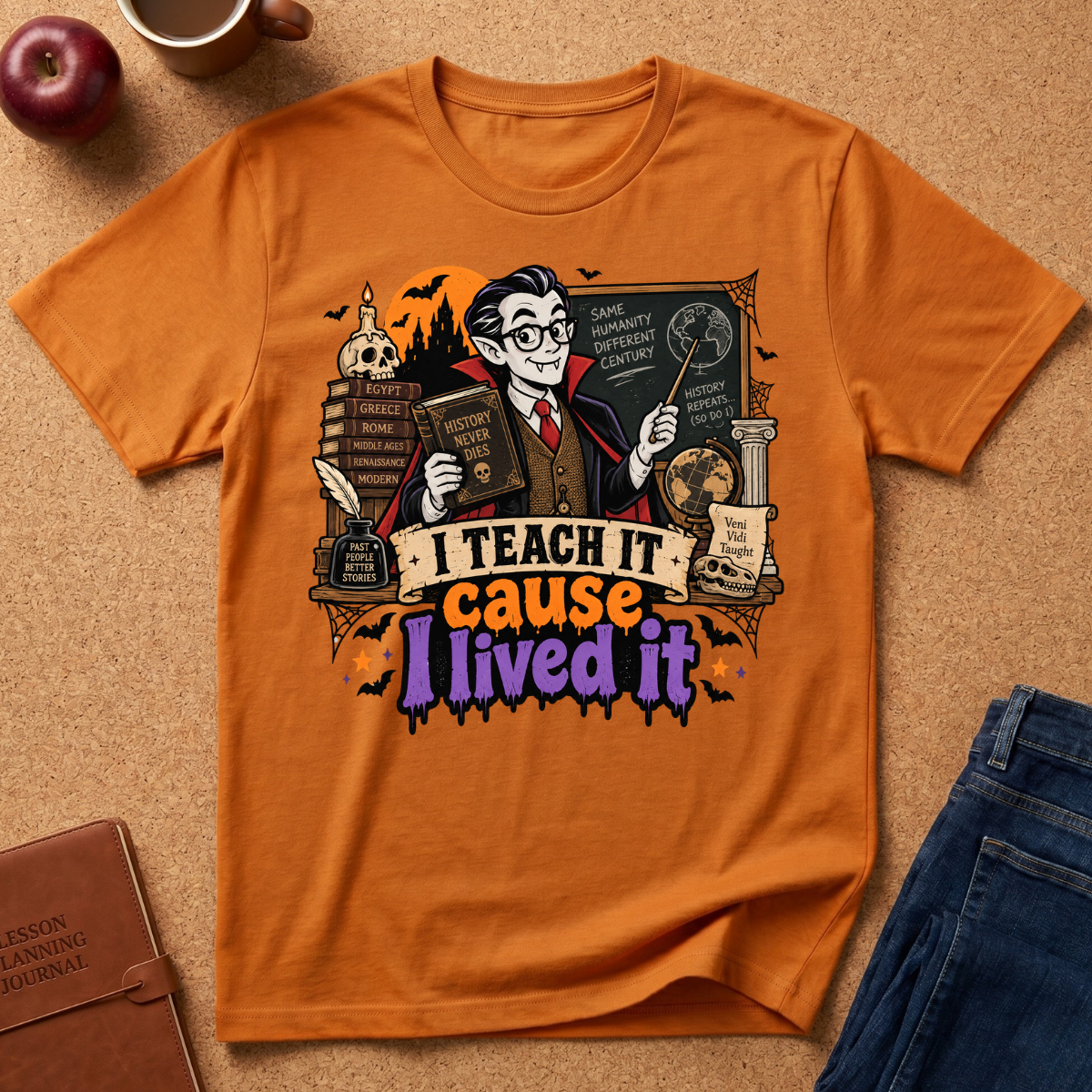 An orange graphic t-shirt laid flat on a cork background, styled with a brown leather journal, a red apple, a coffee mug, and blue jeans. The t-shirt features a detailed graphic of a nerdy cartoon character holding books and a wand, with the text 'I TEACH IT cause I lived it' in colorful stylized lettering.