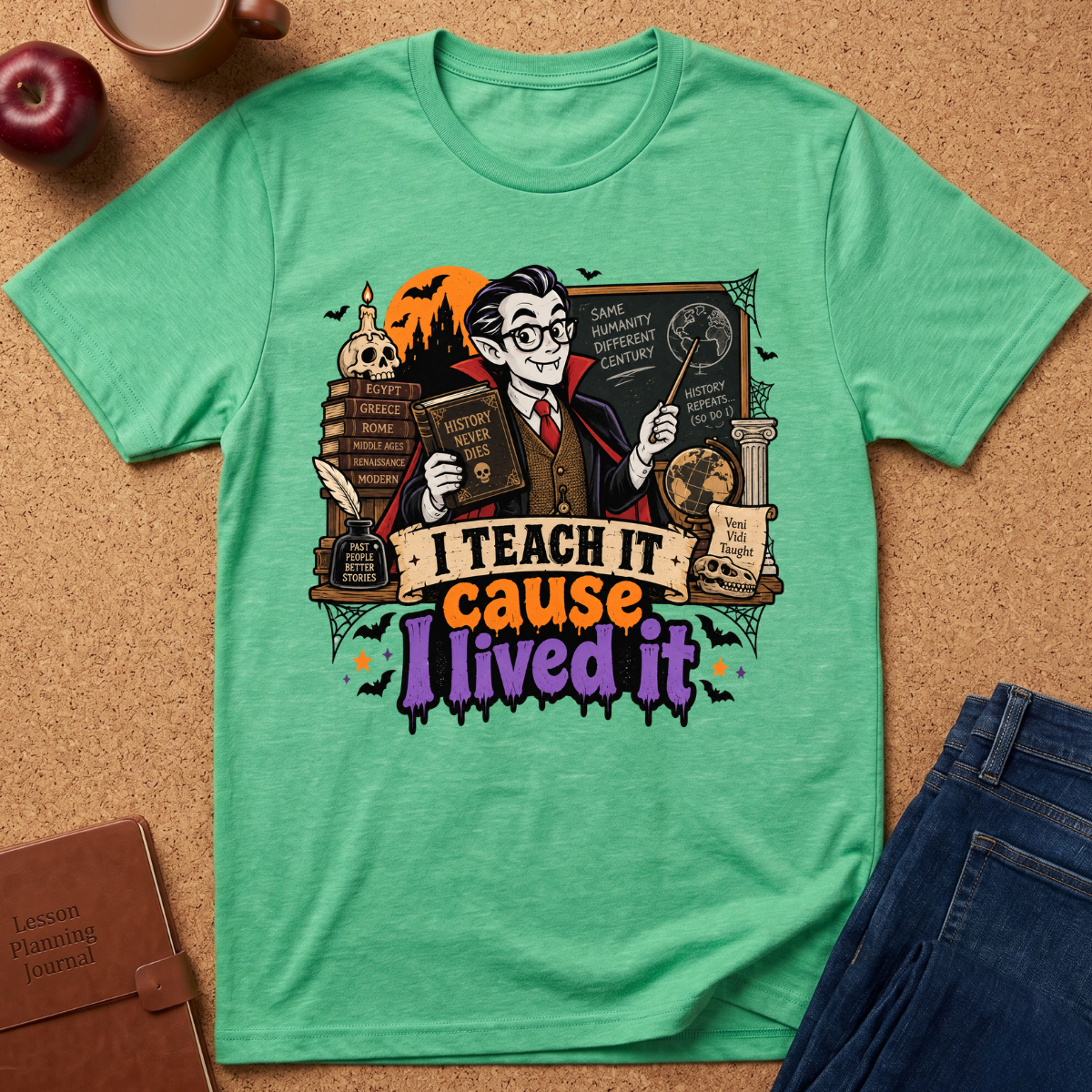 A mint green graphic t-shirt laid flat on a corkboard background, styled with an apple, coffee cup, notebook, and jeans. The t-shirt features a colorful graphic of a cartoon teacher holding books and a chalkboard, with the text 'I TEACH IT cause I lived it'.