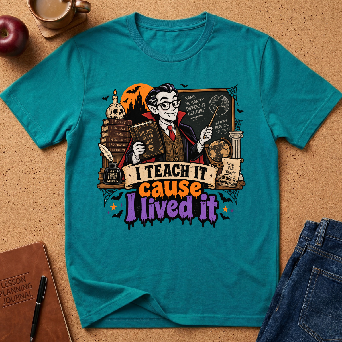 A teal short-sleeve graphic T-shirt laid flat on a cork surface with styled props including an apple, coffee cup, notebook, pen, and jeans. The shirt features a large illustrated wizard holding books and a wand, with the text 'I TEACH IT cause I lived it' across the front.