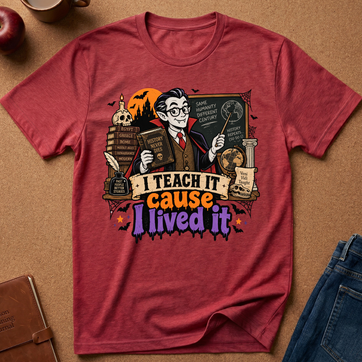 A red graphic t-shirt laid flat on a brown textured surface, featuring a wizard holding a book and wand with the text 'I TEACH IT cause I lived it' in colorful lettering. Styled flat-lay props include jeans, an apple, a notebook, and a mug around the shirt.