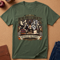 An olive green short-sleeve t-shirt with a detailed Halloween-themed graphic print featuring skeletons, books, and the text 'Dead Poets Society' and 'Checked Out for Eternity', laid flat on a cork background with lifestyle props.