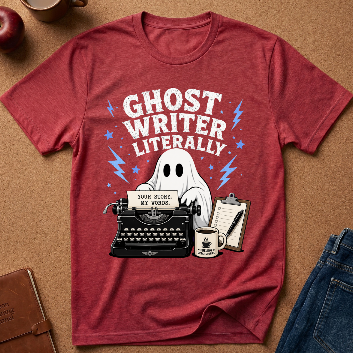 A red heather graphic t-shirt laid flat on a brown cork background, featuring a white ghost, typewriter, coffee mug, and the text 'GHOST WRITER LITERALLY'.