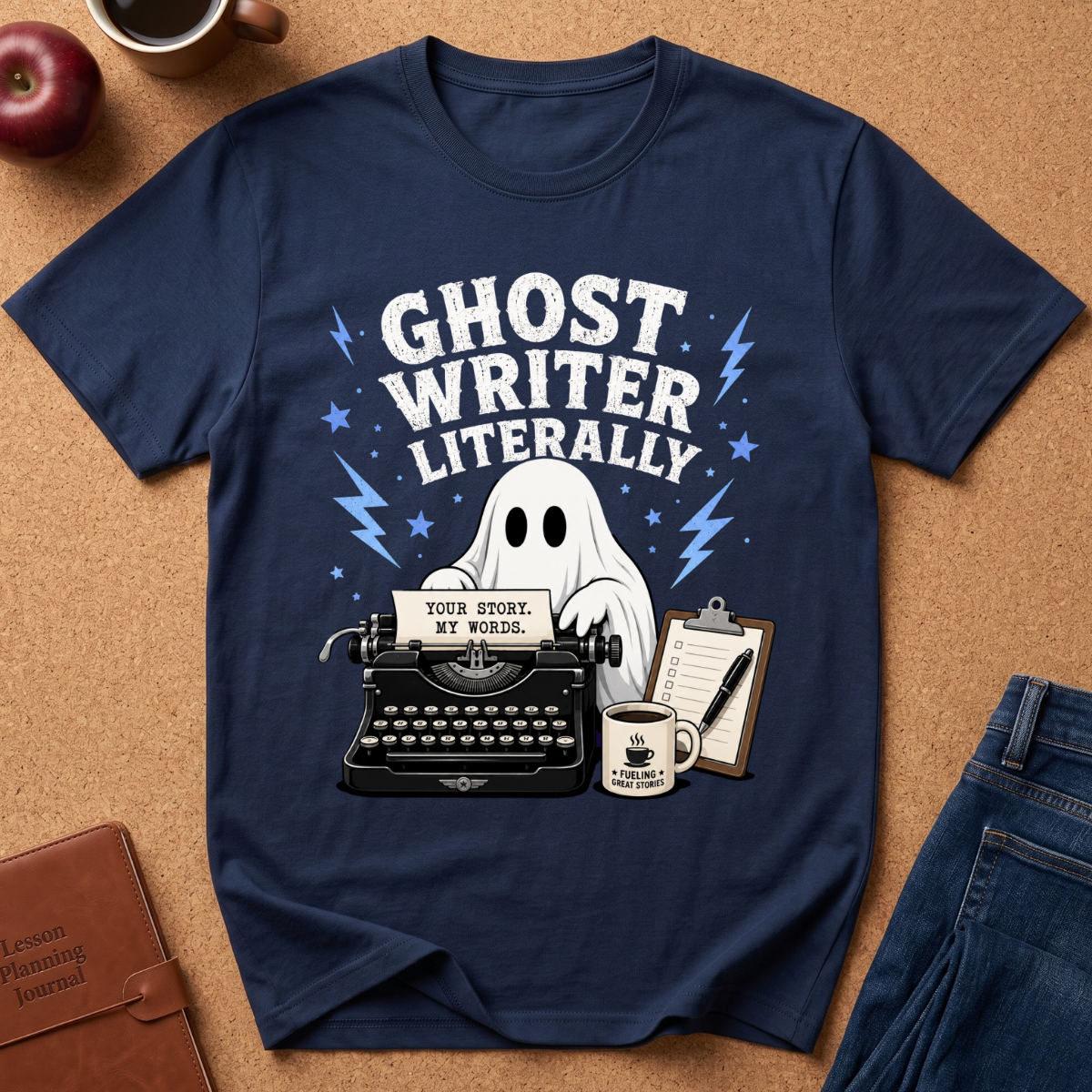 A navy blue graphic t-shirt laid flat on a brown cork background, featuring a ghost writer illustration with a typewriter, coffee mug, and the text 'GHOST WRITER LITERALLY'.