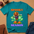 tropicl blue Spooky Season Pumpkin T-Shirt pairs a grinning jack-o’-lantern rising through green mist with scattered pumpkins and bold retro “SPOOKY SEASON” lettering. 