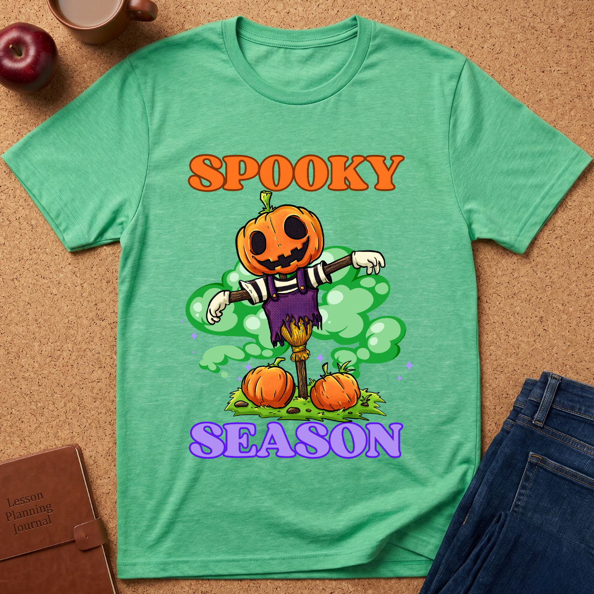 Hether green Spooky Season Pumpkin T-Shirt pairs a grinning jack-o’-lantern rising through green mist with scattered pumpkins and bold retro “SPOOKY SEASON” lettering. 