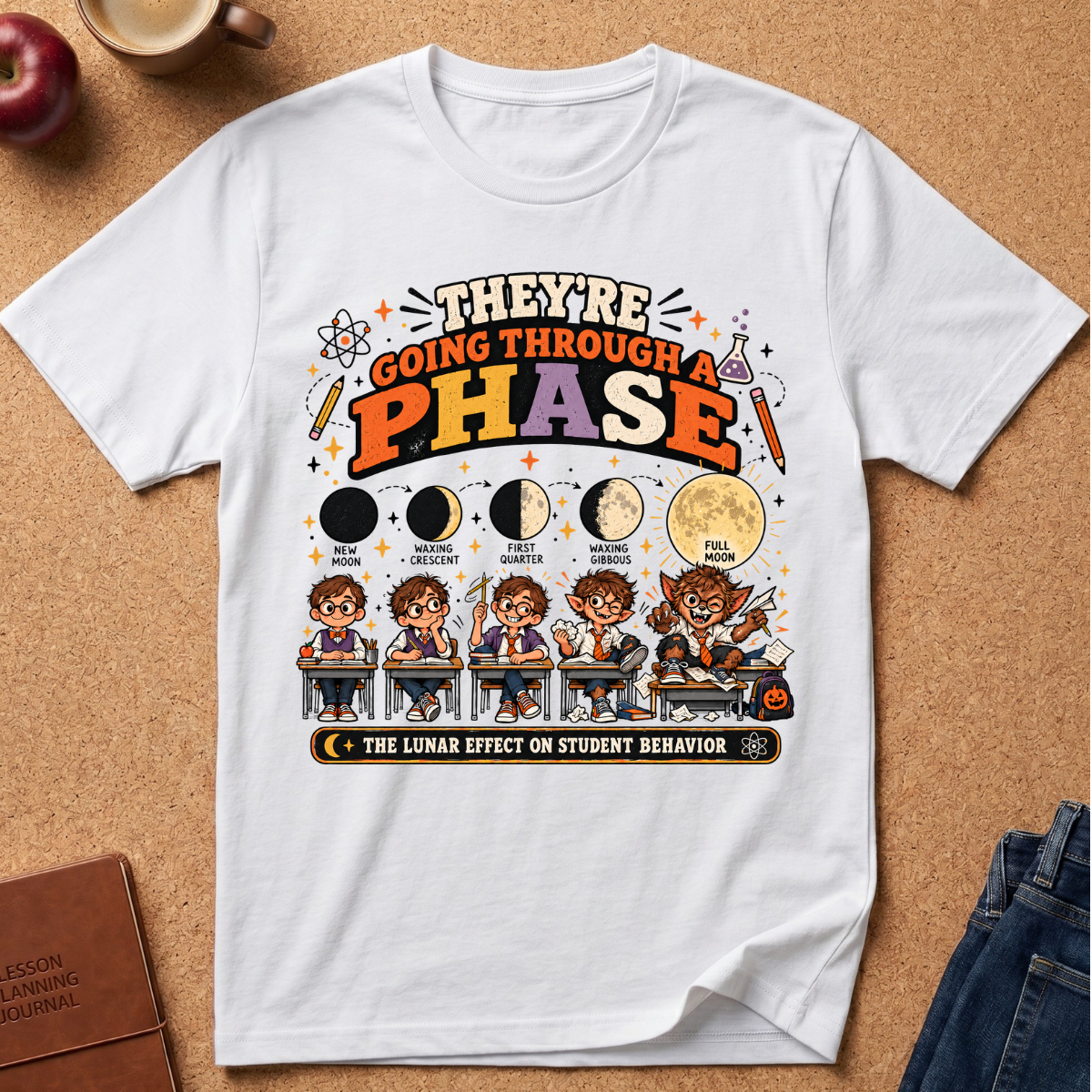 A white short-sleeve graphic T-shirt laid flat on a cork background, featuring a colorful educational poster-style print about the lunar effect on student behavior with moon phases, cartoon students, and decorative text.