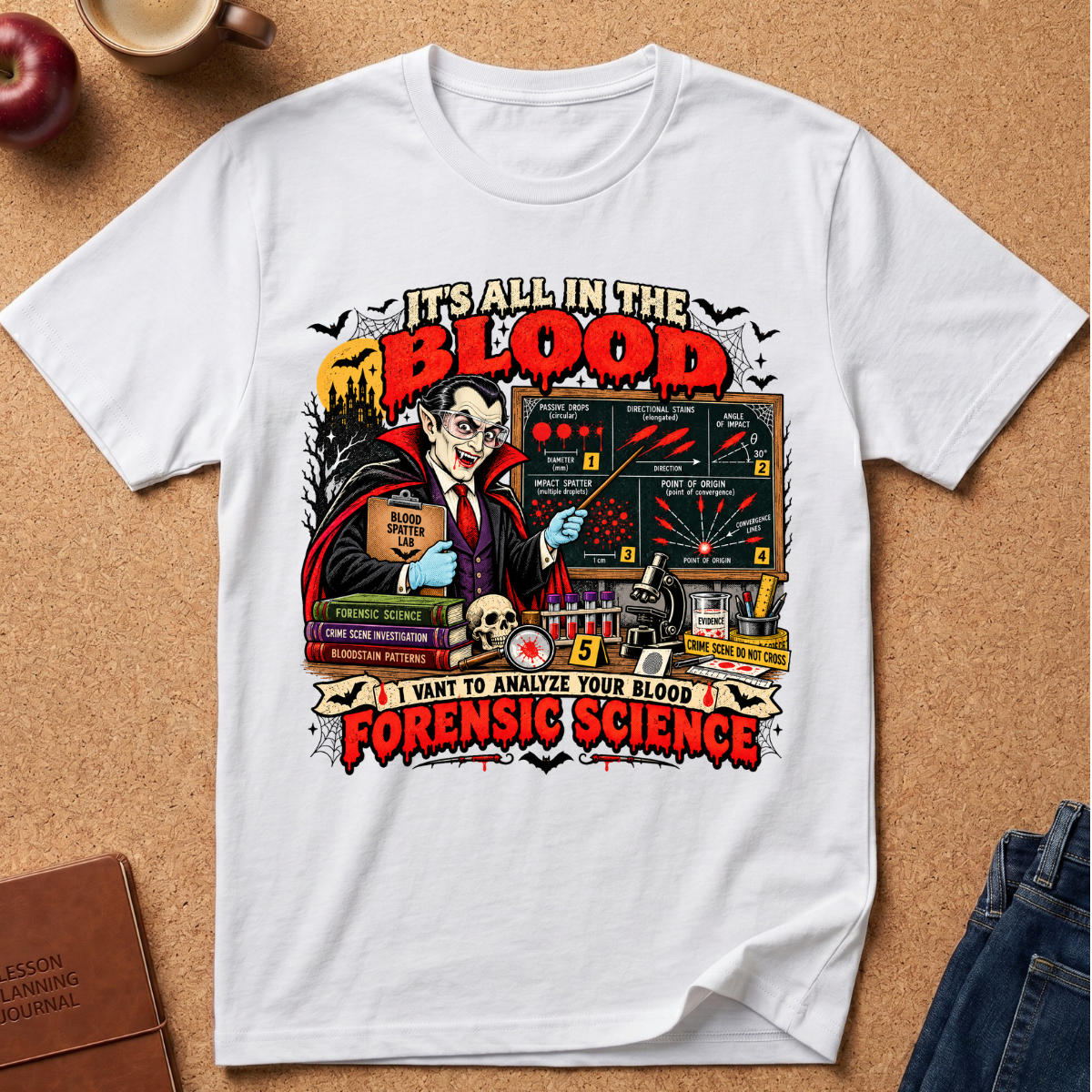A white short-sleeve graphic T-shirt laid flat on a cork board background, surrounded by styled props including an apple, a coffee cup, a journal, and folded jeans. The shirt features a large colorful vintage-style illustration with the text 'IT'S ALL IN THE BLOOD' and 'I WANT TO ANALYZE YOUR BLOOD FORENSIC SCIENCE.