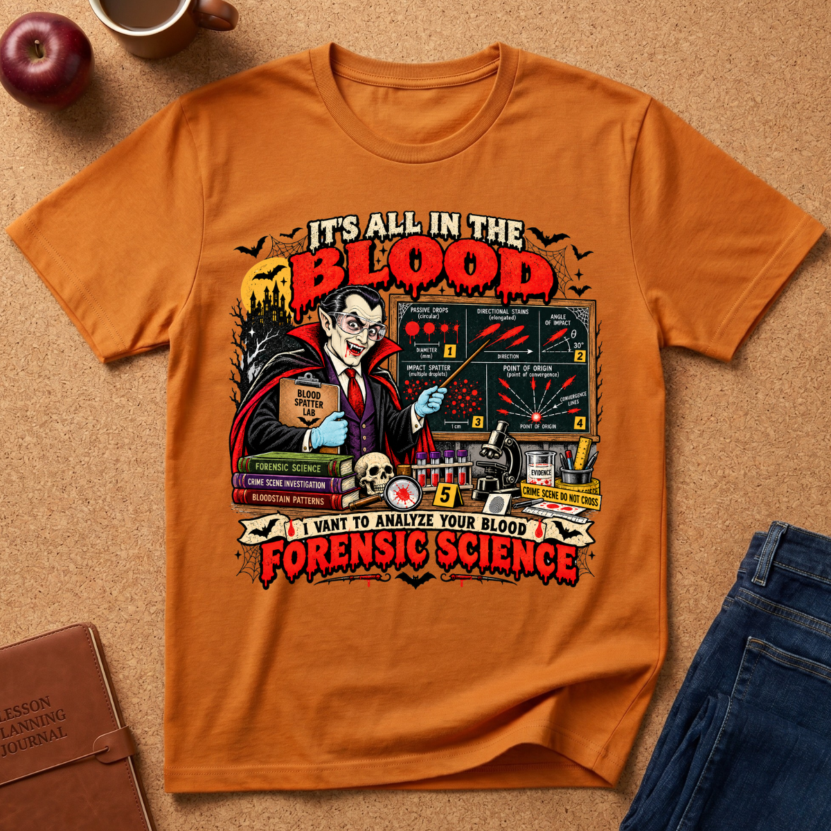 An orange graphic t-shirt laid flat on a brown cork background, styled with a coffee mug, apple, leather journal, and blue jeans. The shirt features a detailed horror-themed graphic with Dr.